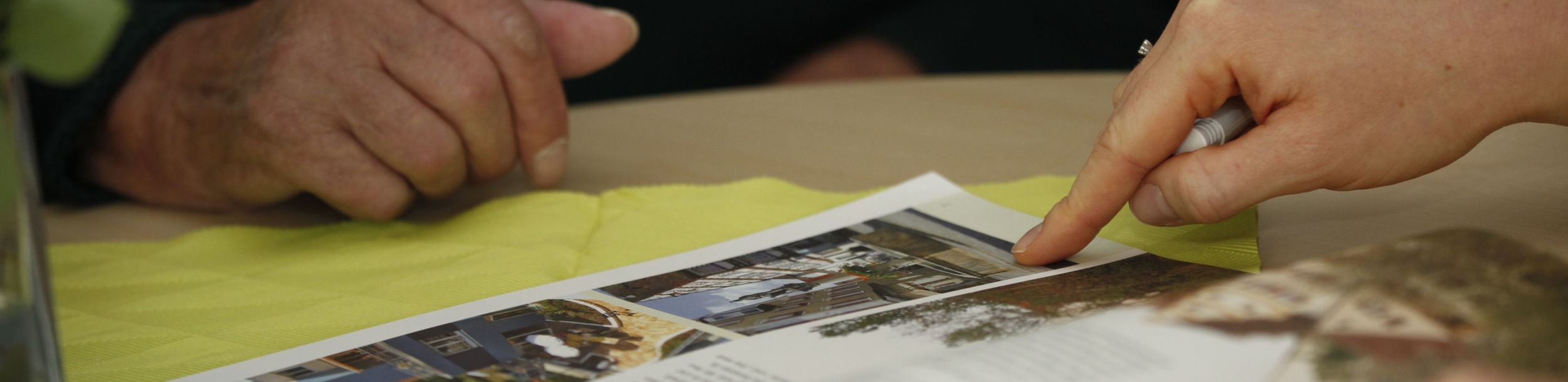 Zwei Hände zeigen auf Fotos in offenem Fotobuch auf dem Tisch