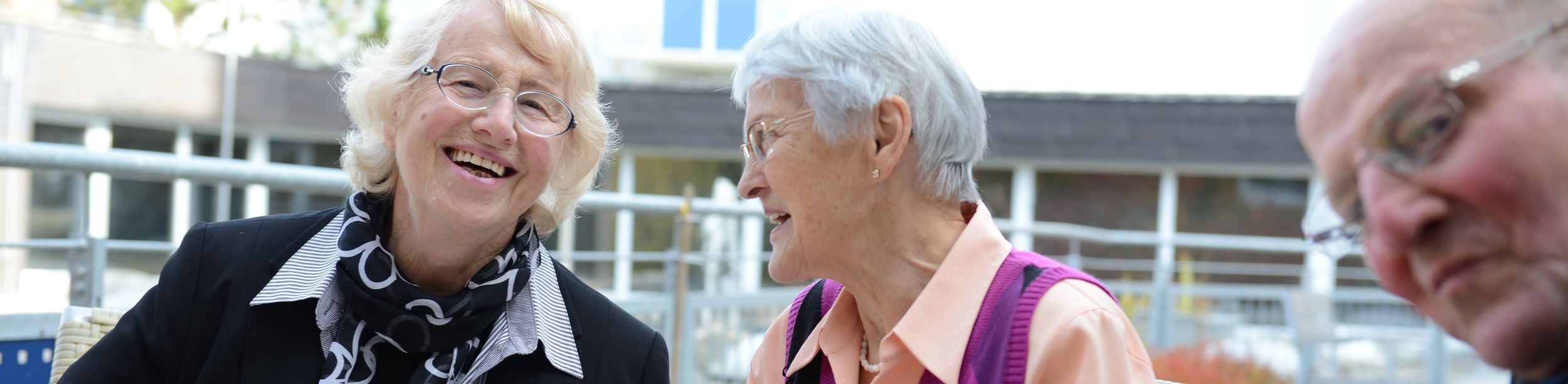 Zwei ältere Frauen lachen beim Kuchenessen auf einer Terrasse