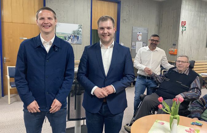 Drei lächelnde Männer, ein älterer Mann im Rollstuhl bei Vorstellungsrunde der Bürgermeisterkandidaten