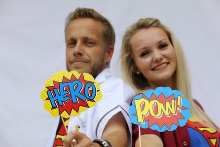 Zwei Personen lächelnd mit Comic-Schildern HERO und POW