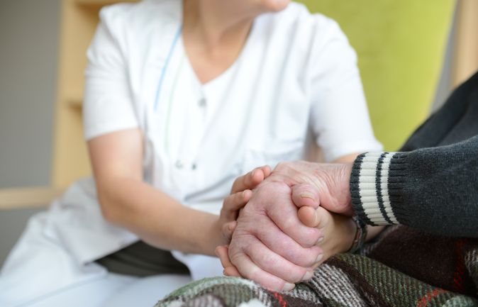 Pflegekraft hält unterstützend die Hände einer älteren Person