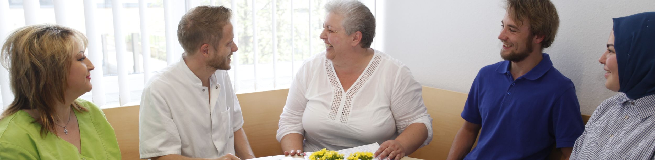 Fünf Personen lächeln bei einem Gespräch an einem Tisch mit Ordnern