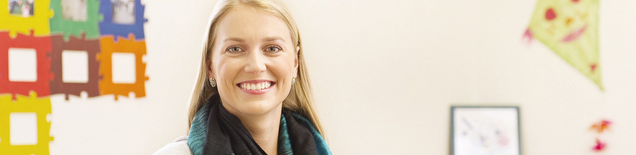 Lächelnde Frau mit blaugrünem Schal vor farbiger Kinderzimmerdeko