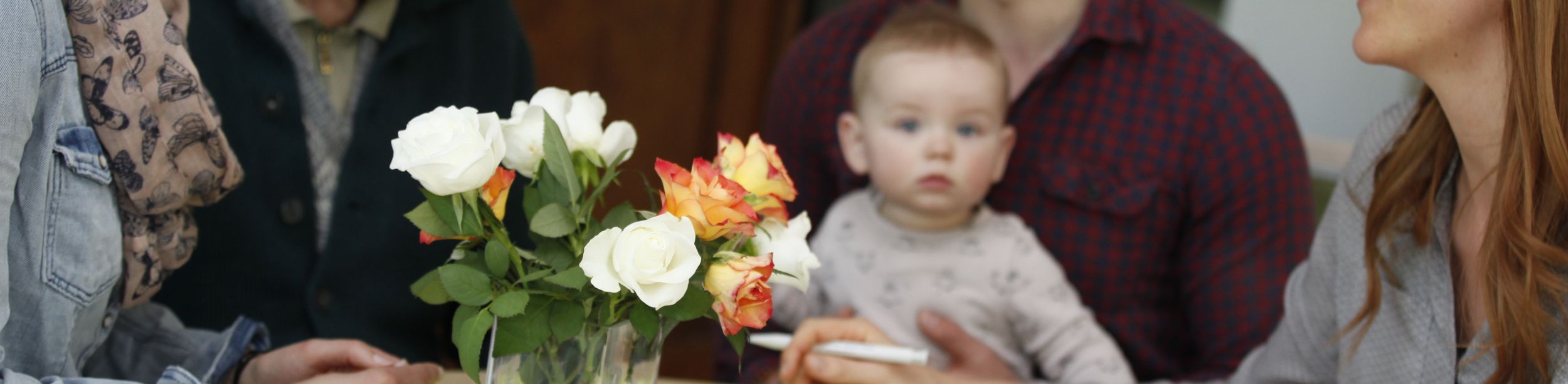Gruppe aus älterem Mann, Baby und drei Erwachsenen am Tisch mit Rosen