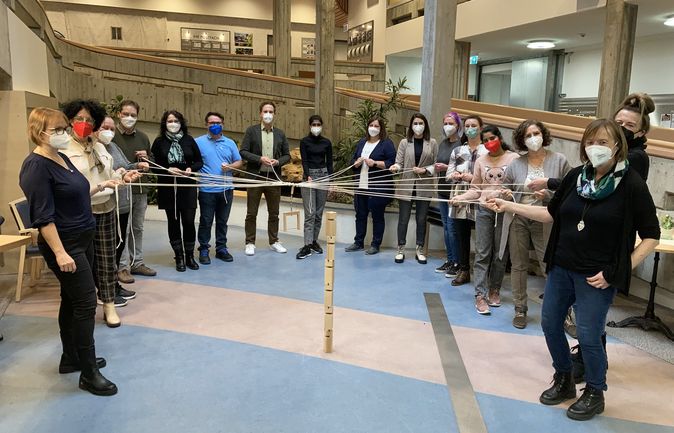 Gruppe mit Masken hält Seile um Holzturm beim Welcome Day